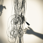 A tangled mass of vintage telephone wires with a shadow hand reaching for the wires.